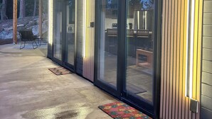 Un edificio moderno con techo de madera, grandes puertas de cristal, patio de hormigón y mobiliario exterior.