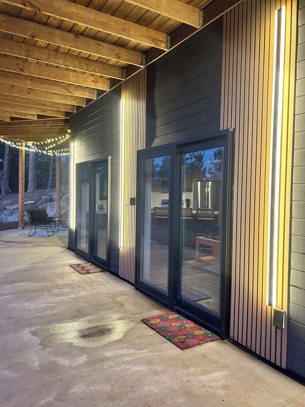 Guests can enjoy a covered patio area with seating and a doormat, accessible through large glass doors and windows.