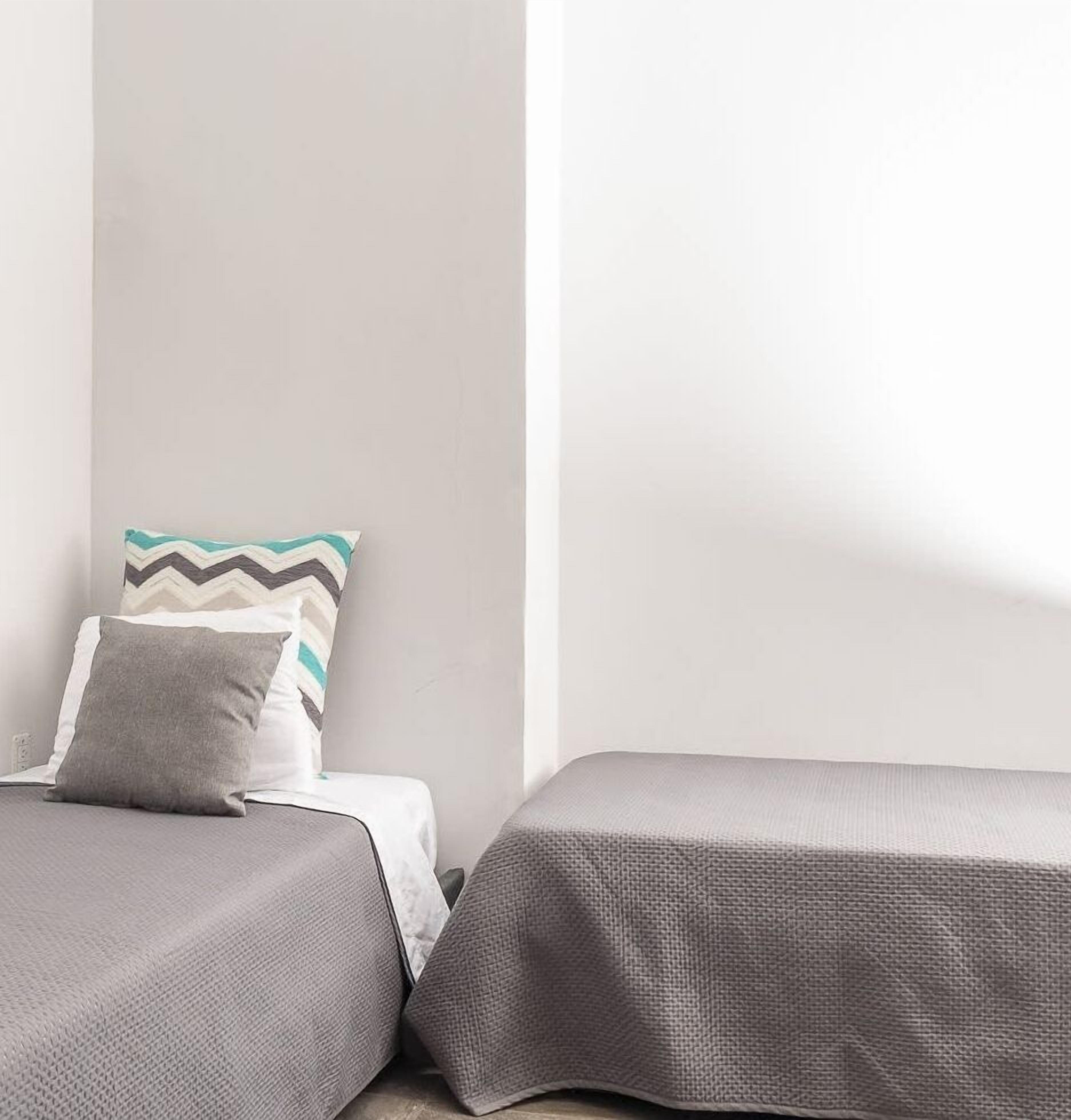 A bedroom with two beds, each with a grey bedspread and pillows.