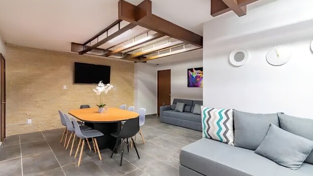 A modern living space with a dining area, a grey sofa, and a television mounted on the wall.