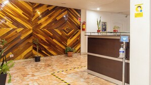 A reception area with a wooden chevron wall, a reception desk, a fire extinguisher, and a hand sanitizer dispenser.