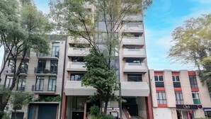 A multi-story building with balconies, a central entrance, and a shop on the ground floor.