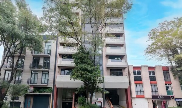 A multi-story building with balconies, a central entrance, and a shop on the ground floor.