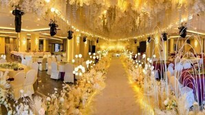 Un salón de banquetes con mesas redondas, sillas blancas y una alfombra decorada con flores.