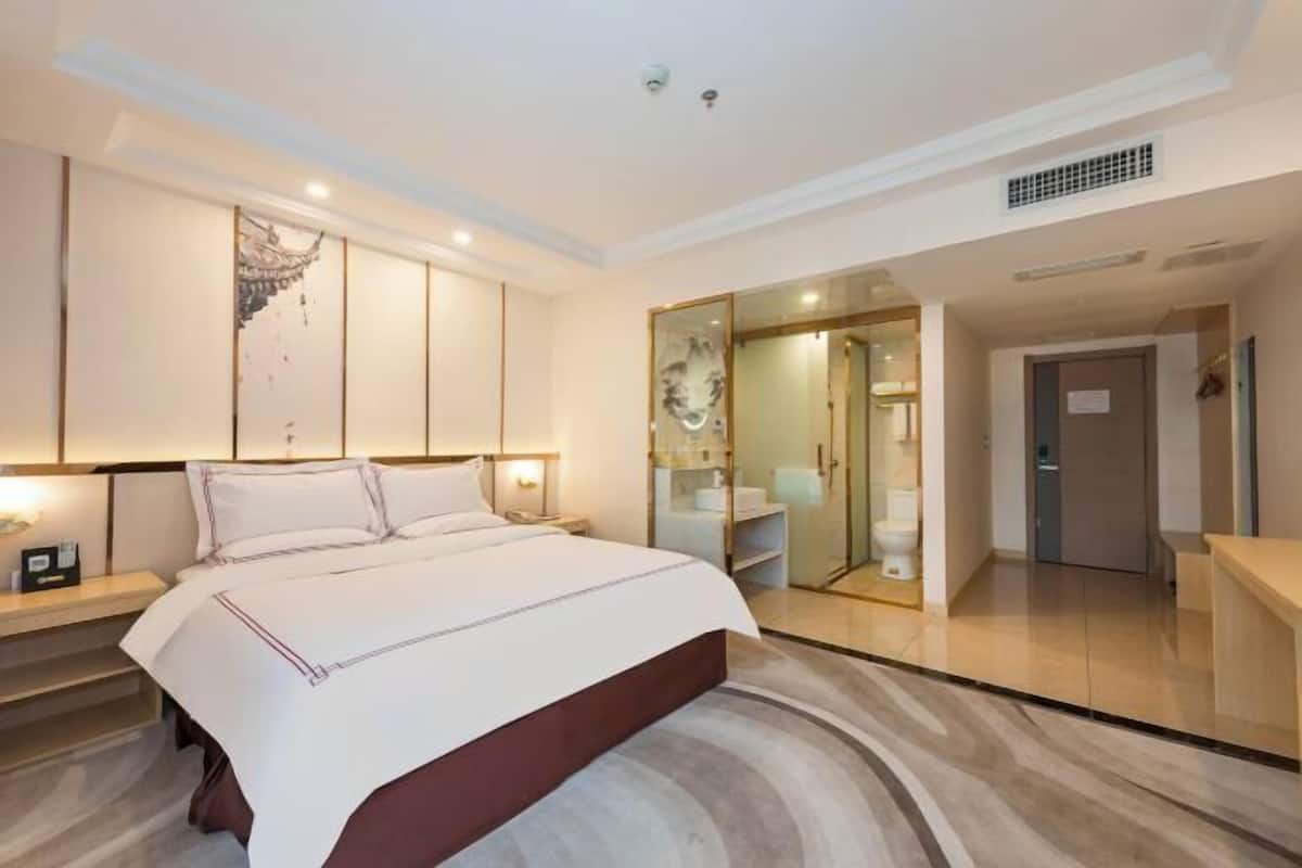 Una habitación de hotel con una cama grande, un vestidor y un baño con cabina de ducha de vidrio.