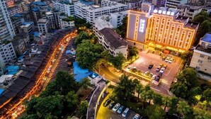 Un hotel urbano con estacionamiento, rodeado de edificios altos y una calle concurrida.