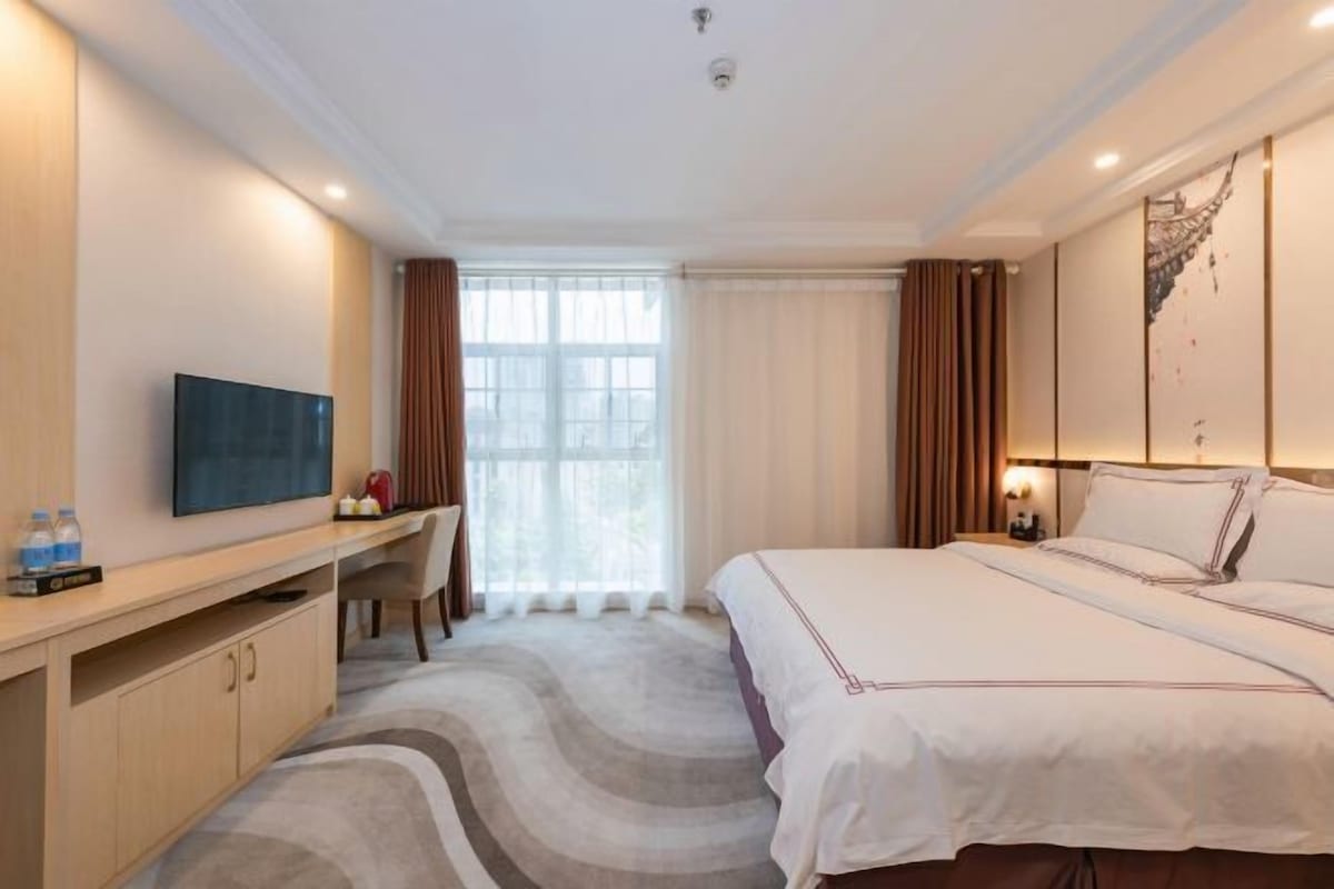 A hotel room with a bed, a desk, a television, and a window with curtains.