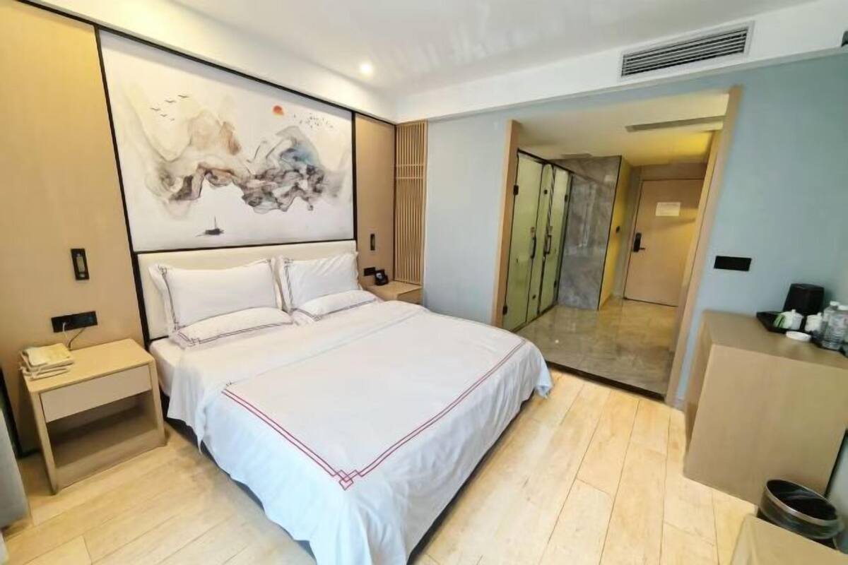 Una habitación de hotel con una cama grande, una mesita de noche, un armario y un espejo.