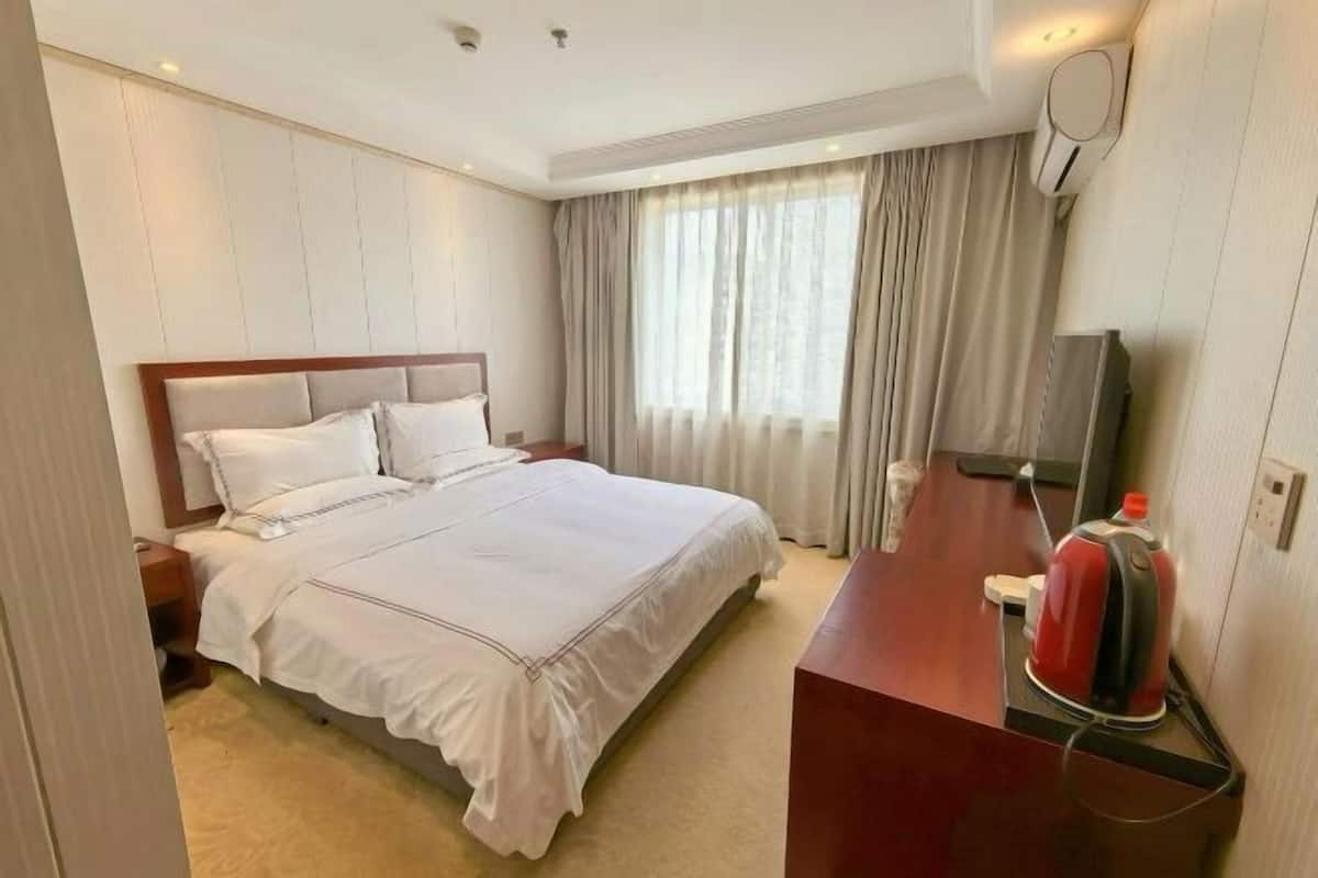 Habitación de hotel con cama, escritorio con hervidor, televisión y ventana con cortinas.