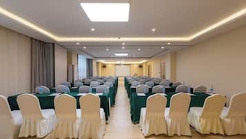 A conference room with rows of tables and chairs, a projector screen, and a long table at the front.