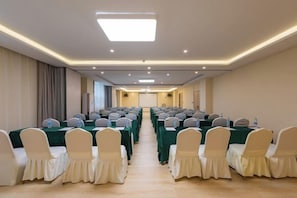 Une salle de conférence avec des rangées de tables et de chaises, un écran de projection et une longue table à l’avant.