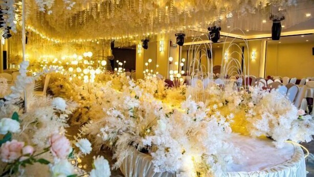 Un salón de banquetes con un centro de mesa floral, candelabros y un escenario.