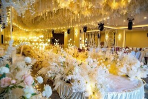 Un salón de banquetes con un centro de mesa floral, candelabros y un escenario.