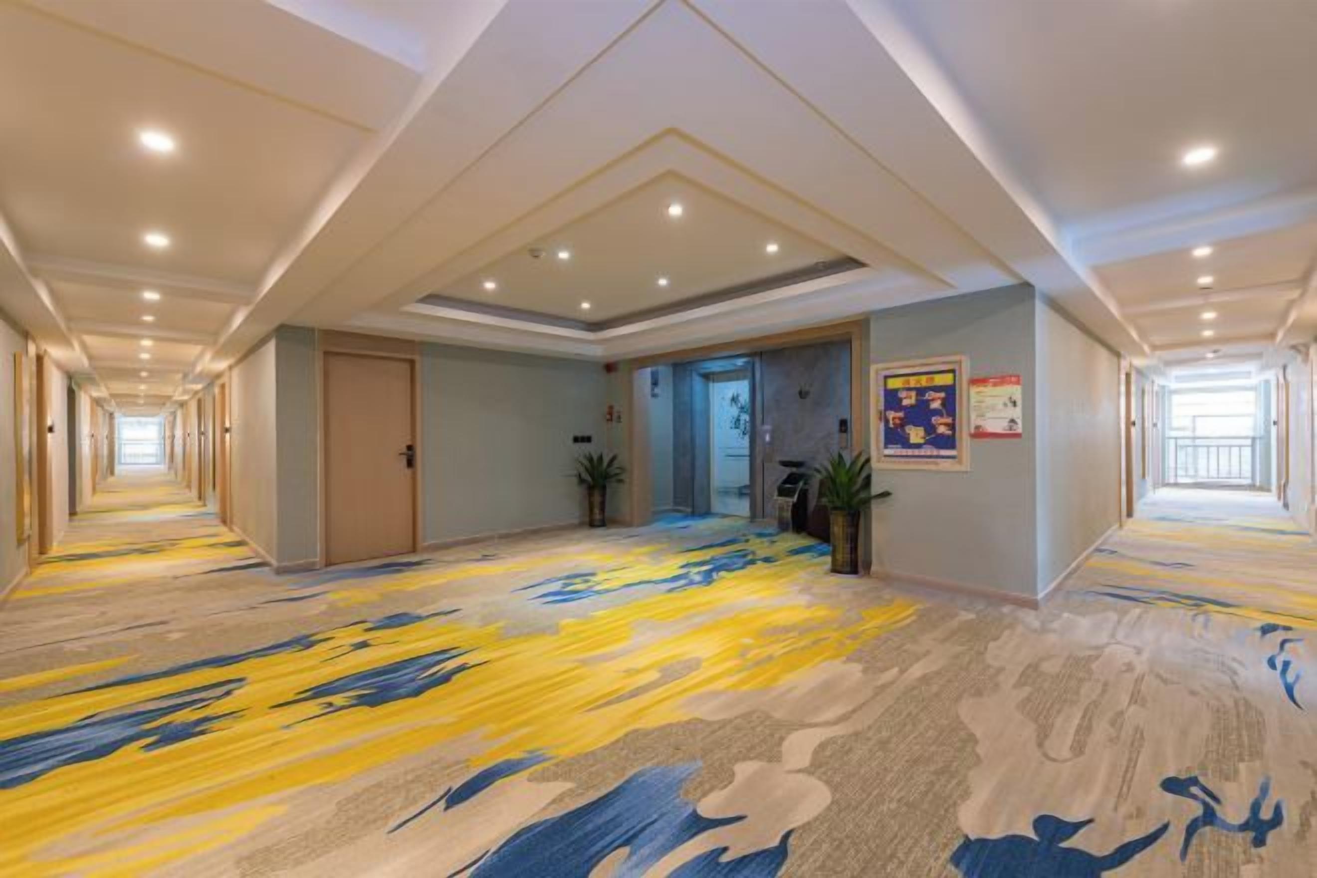 A hotel corridor with a patterned carpet, recessed lighting, and a door leading to a room.