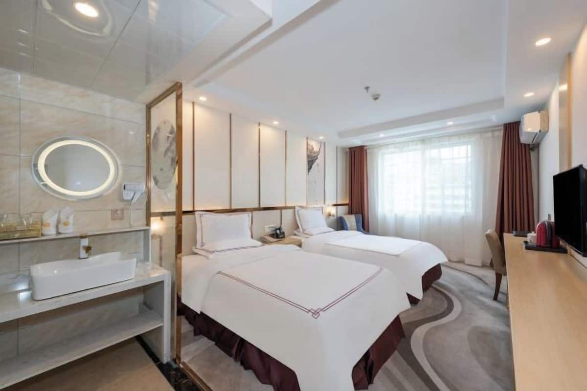 Una habitación de hotel con dos camas, un espejo grande, un televisor y un baño con lavabo y tocador.