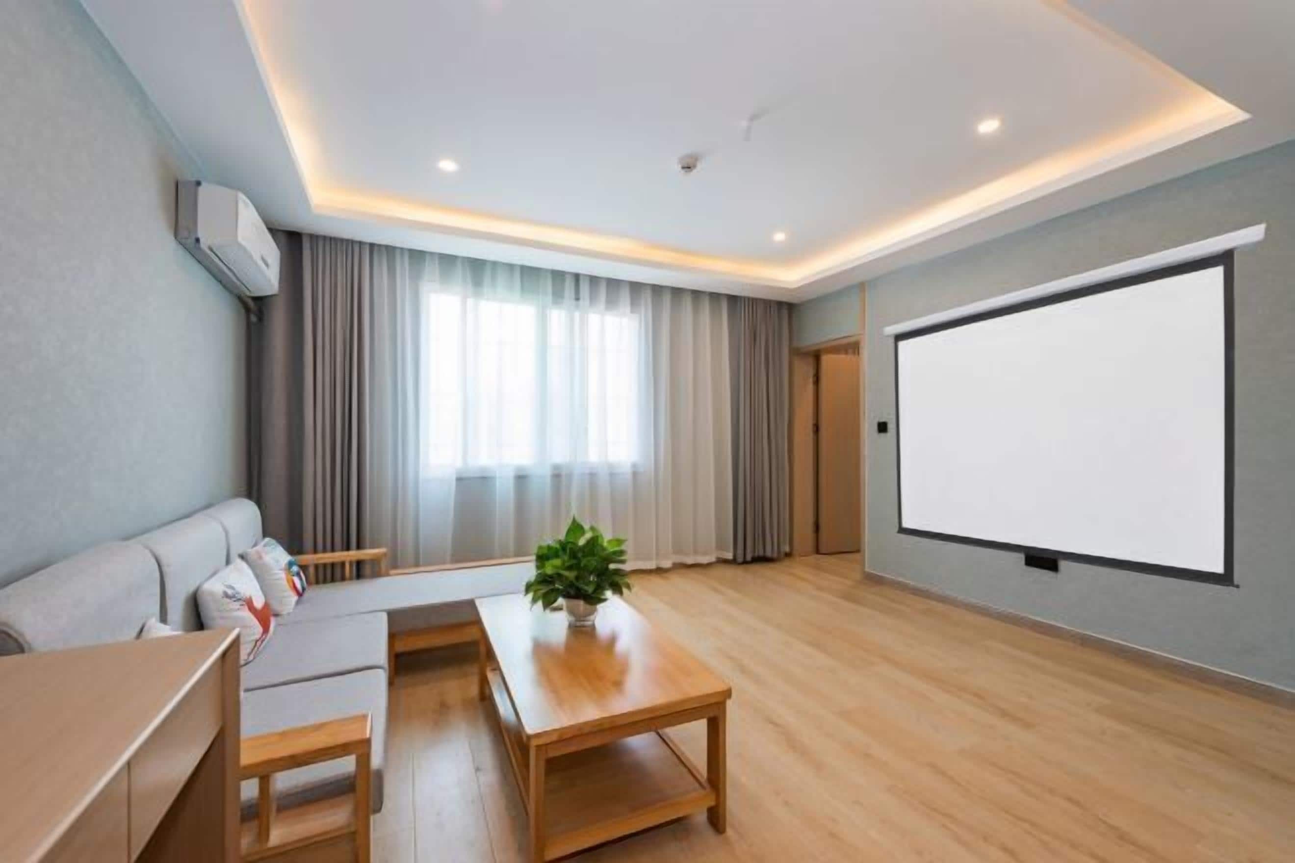 Una sala de estar moderna con un sofá, una mesa de centro, una pantalla de televisión y un ventanal grande con cortinas.