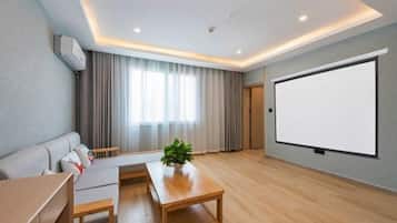 Una sala de estar moderna con un sofá, una mesa de centro, una pantalla de televisión y un ventanal grande con cortinas.