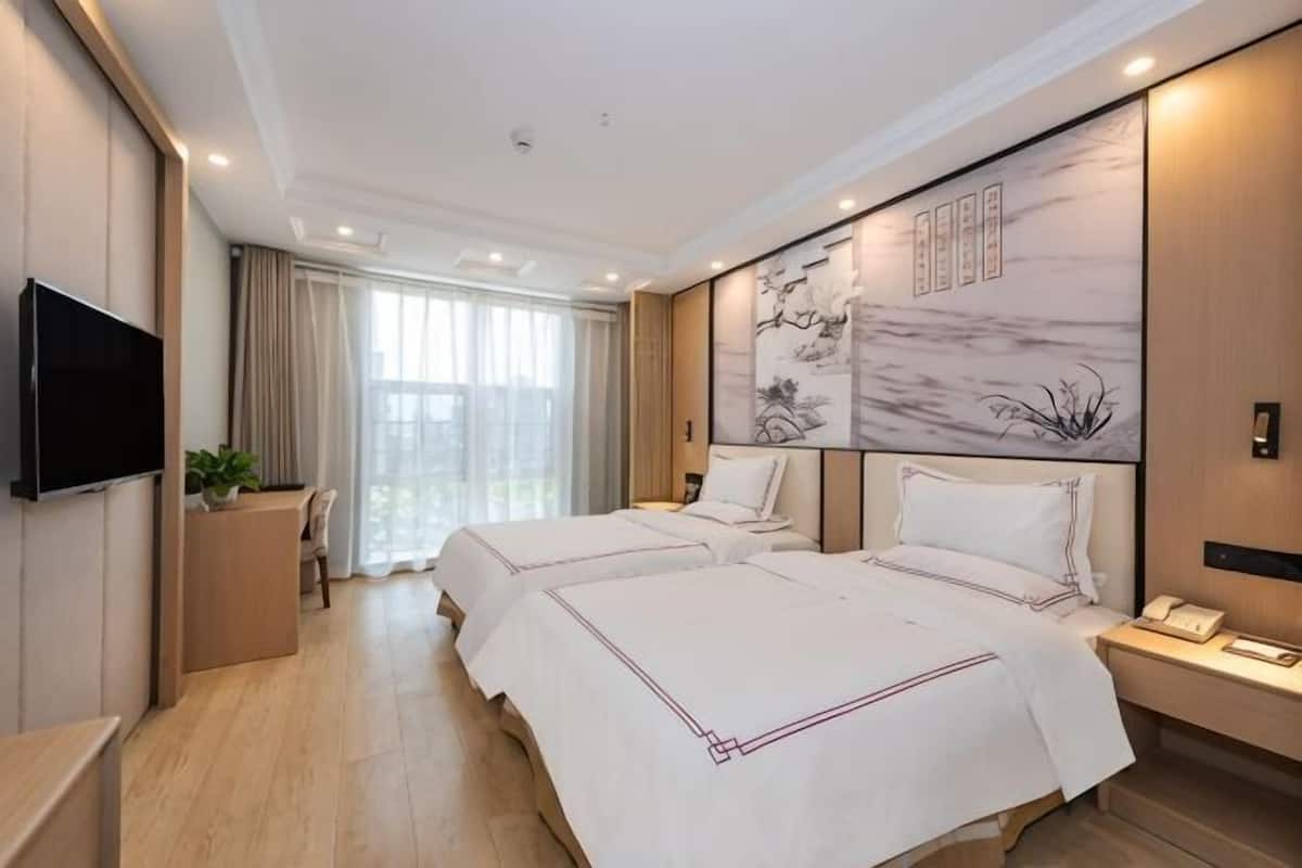 Habitación de hotel con dos camas, un escritorio, un televisor y un ventanal amplio.