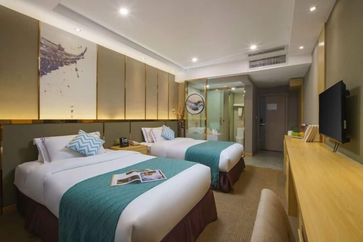 Una habitación de hotel con dos camas, un escritorio de madera, un televisor y obras de arte en las paredes.