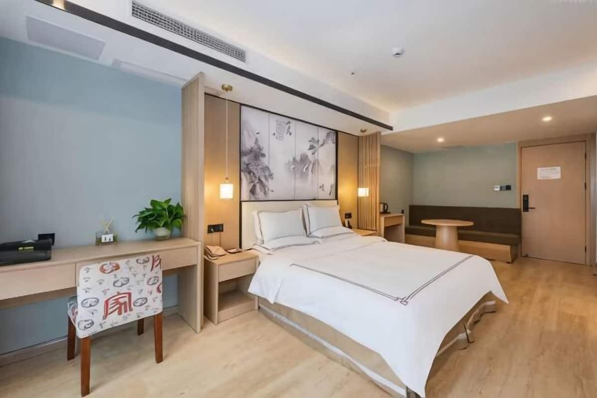 Una habitación de hotel con cama, escritorio, silla, mesitas de noche y una pequeña mesa.