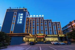 A hotel with a prominent entrance, multiple floors, and a parking lot with several cars. - Qiao Cheng Hotel (Duyun)
