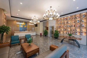 Een hotel lobby met een receptiebalie, een zithoek, boekenkasten en een kroonluchter.