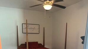 A bedroom with a four-poster bed, a ceiling fan, and a framed quote on the wall.