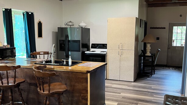 A kitchen with a wooden island, bar stools, a refrigerator, stove, and a ceiling fan.