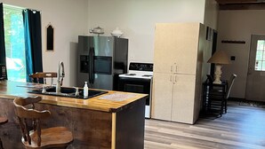 A kitchen with a wooden island, bar stools, a refrigerator, stove, and a cabinet.