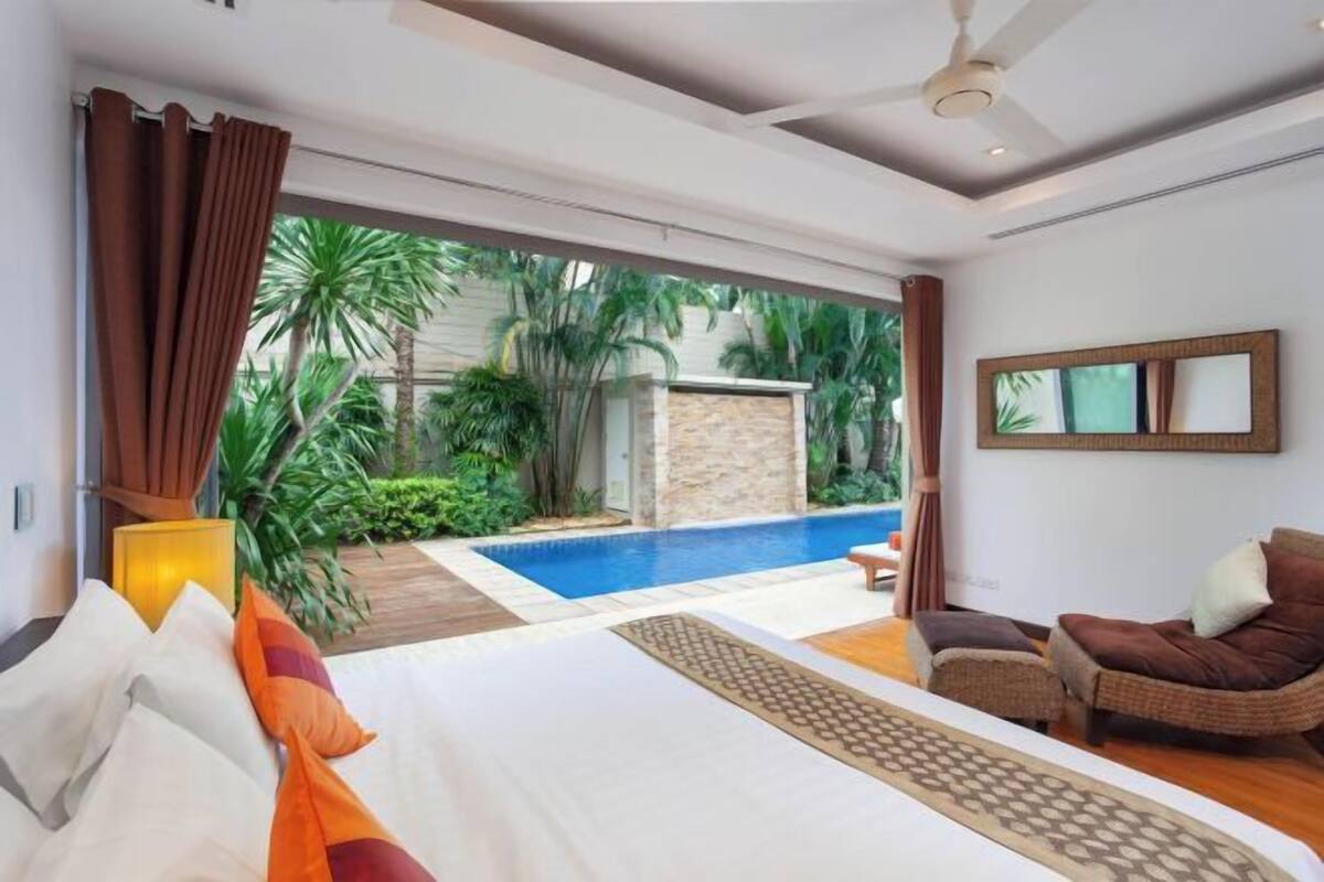 Habitación de hotel con una cama grande, un sofá, un ventilador de techo, vistas a una piscina y una pared de piedra.