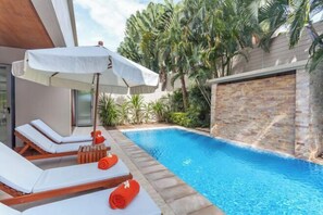 A poolside area with lounge chairs and an umbrella, surrounded by tropical plants. - The Residence Resort (Phuket)