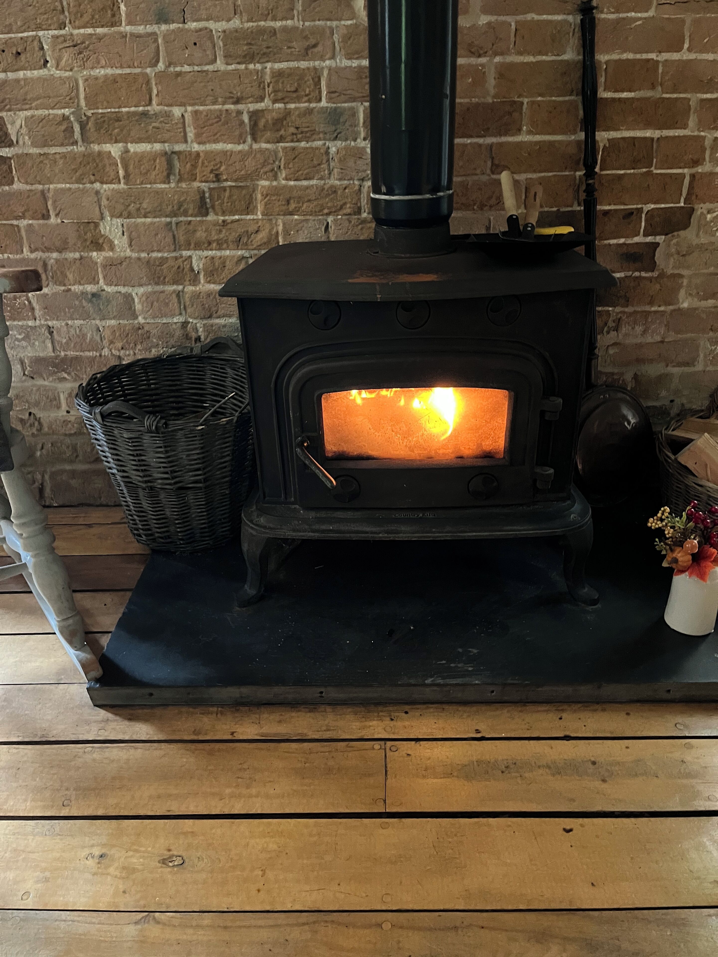 A wood-burning stove with a glass door, a black chimney, and a wicker basket beside it.