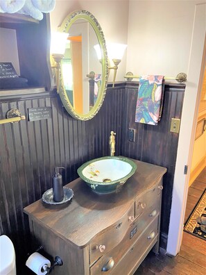 Een badkamer met een houten wastafelmeubel, een groene wasbak, een spiegel en een handdoekrek.