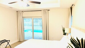 A hotel room with a bed, a chair, a ceiling fan, a window with curtains, and a view of a swimming pool.