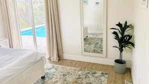 A bedroom with a bed, a large mirror, a potted plant, and a view of a swimming pool through a sliding door.