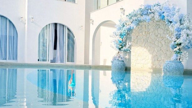 Una piscina con agua azul cristalina, paredes blancas y un arco floral.