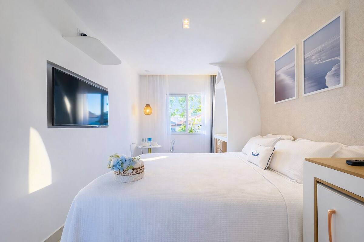Una habitación de hotel moderna con una cama grande, un televisor de pantalla plana, una mesita con un florero y una ventana con vistas al exterior.