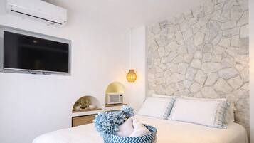 A bedroom with a stone wall, a flat-screen TV, a microwave, and a bedside table with a vase of flowers.