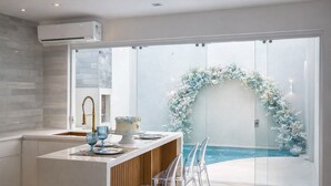 Una cocina moderna con puerta de vidrio que da a una zona de piscina, un comedor y un equipo de aire acondicionado en la pared.