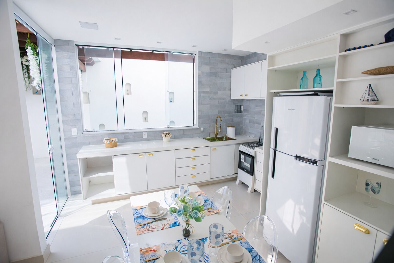 A modern kitchen with white cabinetry, a dining area with a table set for two, and a built-in oven and refrigerator.