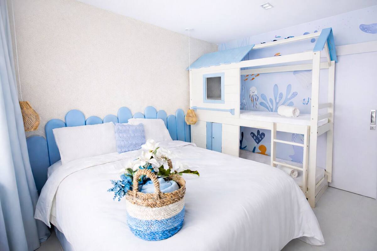 Un dormitorio con una litera, una cama con ropa de cama blanca y una cesta tejida sobre la cama.