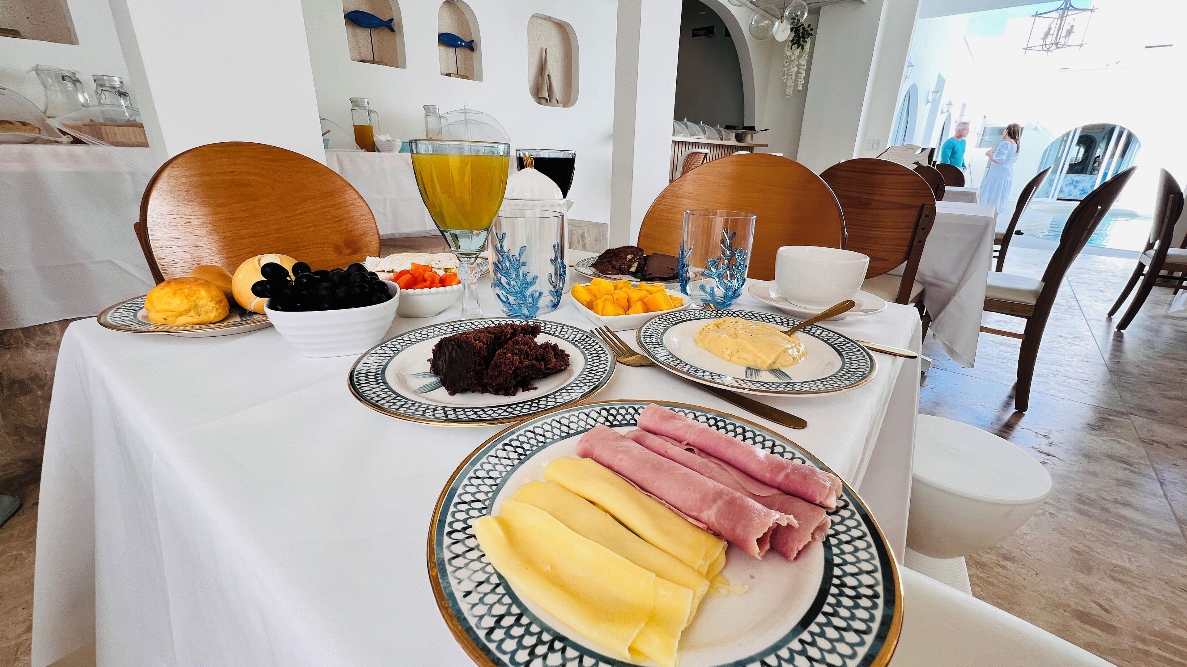 Una mesa de comedor con diversos platos, entre ellos pasteles, frutas y carnes, en una habitación con una decoración moderna y vistas al mar.
