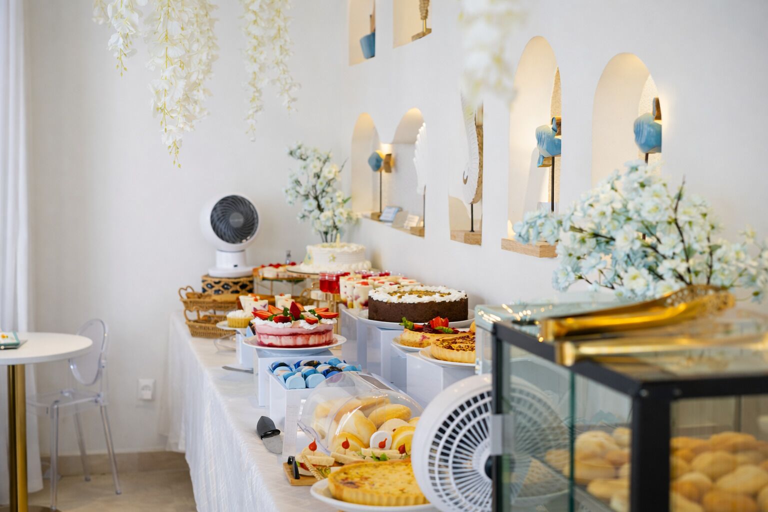 A buffet with various desserts and pastries, including cakes and pies, arranged on a table with a white tablecloth.