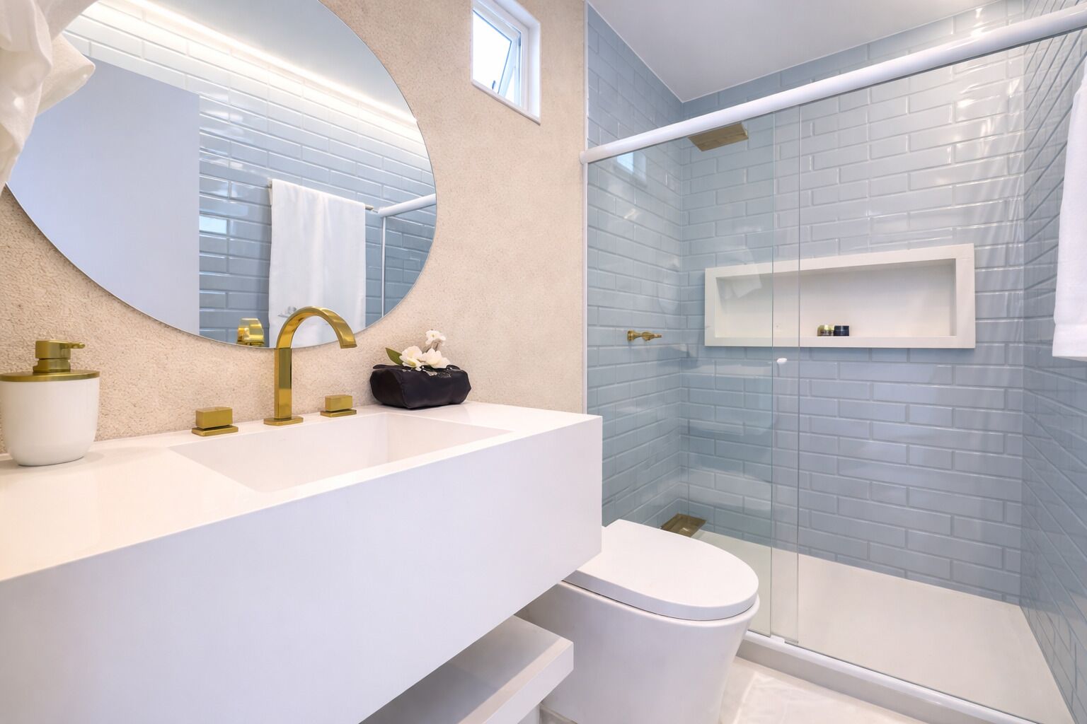 A modern bathroom with a white vanity, gold fixtures, a glass shower enclosure, and a white toilet.