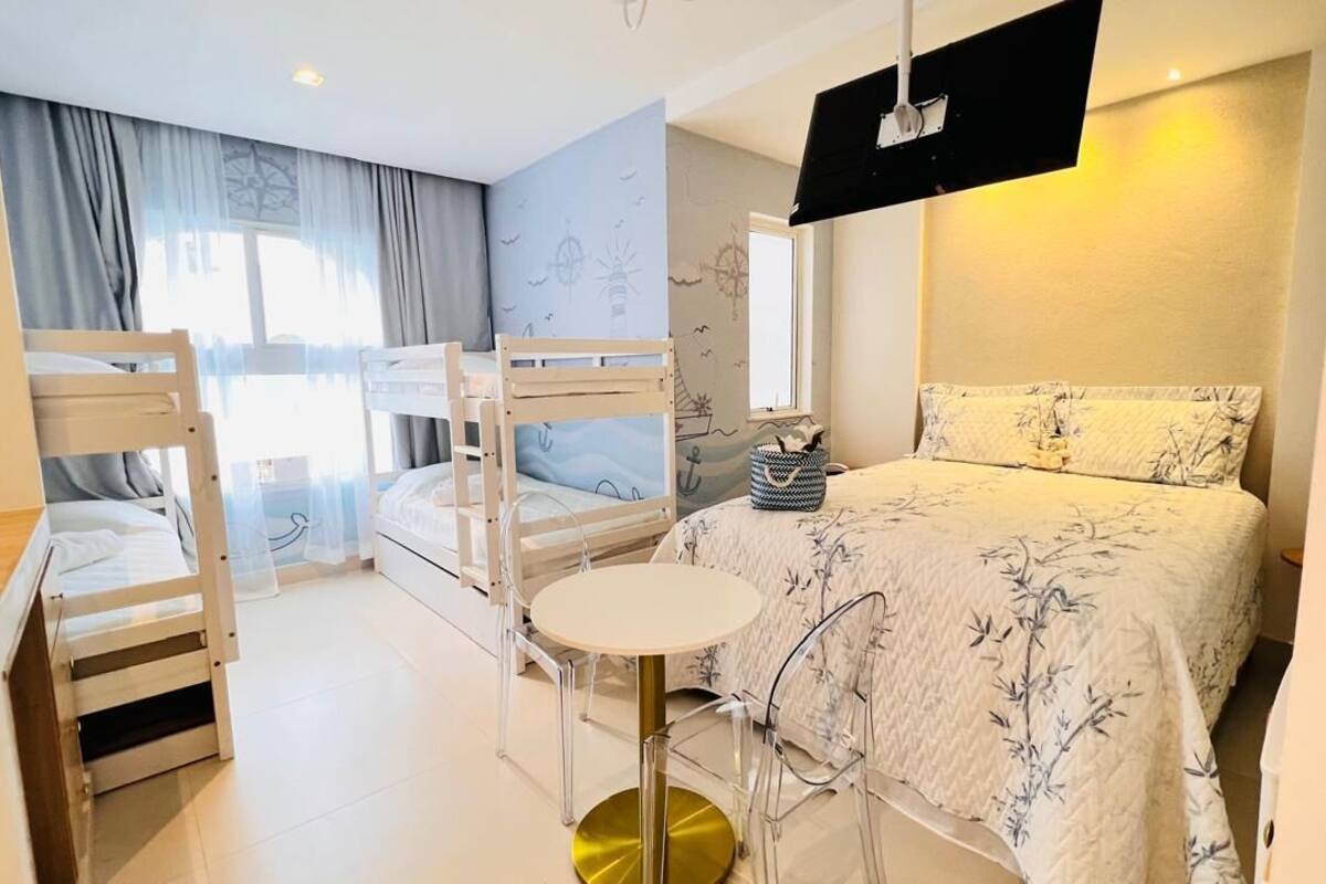Una habitación de hotel con literas, una mesa redonda y una cama con colcha estampada.