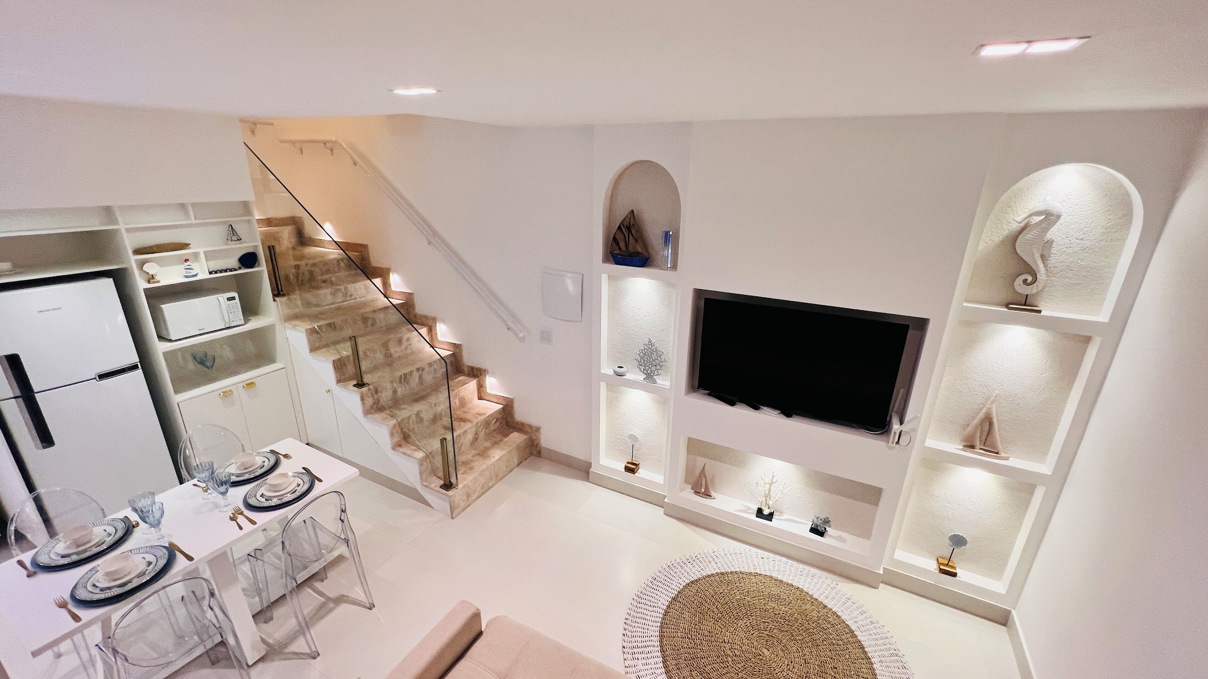 A modern kitchen with a built-in refrigerator, microwave, and stove. There is a dining area with a table set for two, and a staircase leading to an upper level.