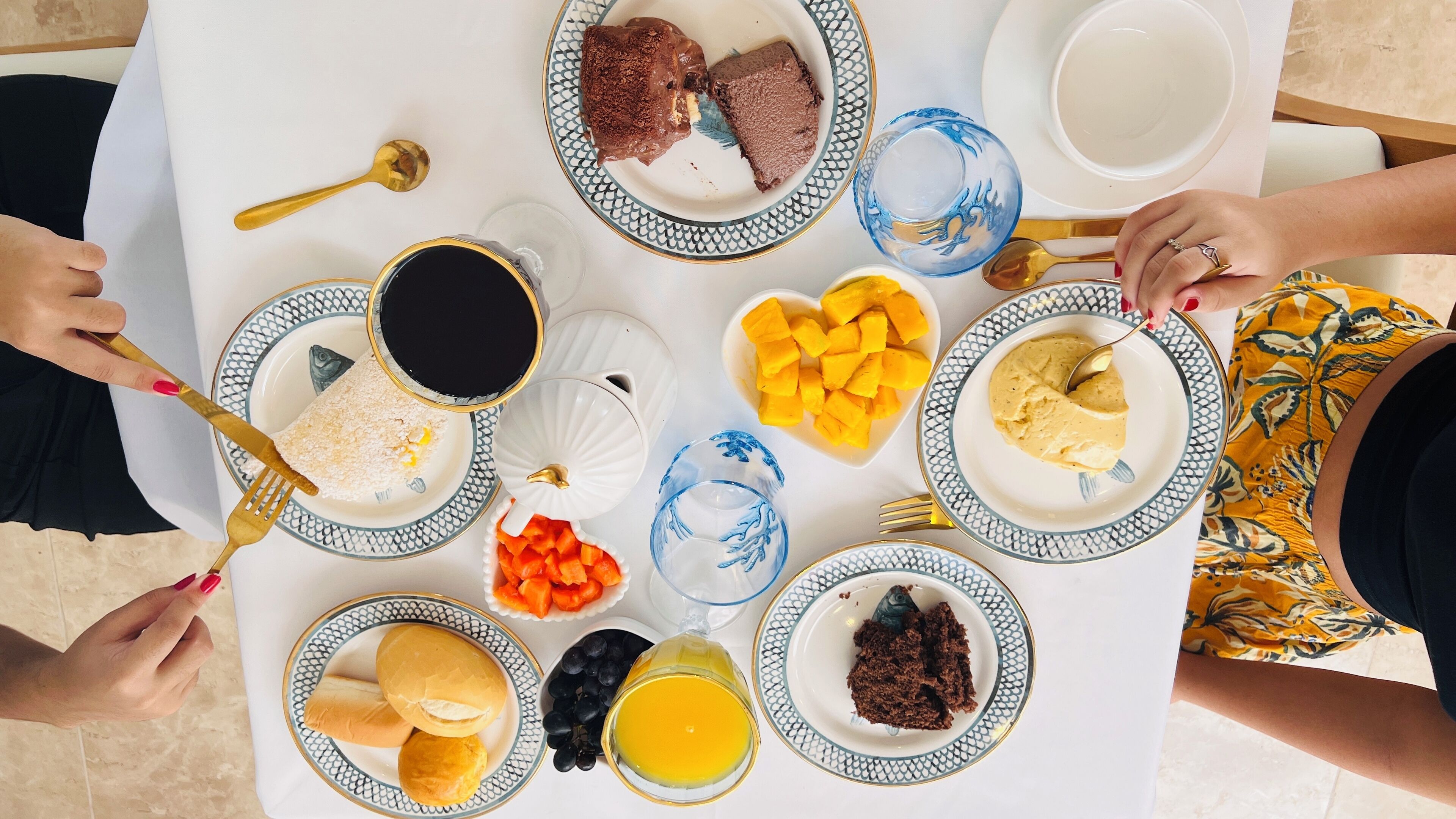 A table set with various dishes including bread, fruit, and a drink, surrounded by people.
