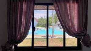 Ένα παράθυρο με κουρτίνες, θέα σε μια πισίνα και ένα κτίριο στο βάθος.
