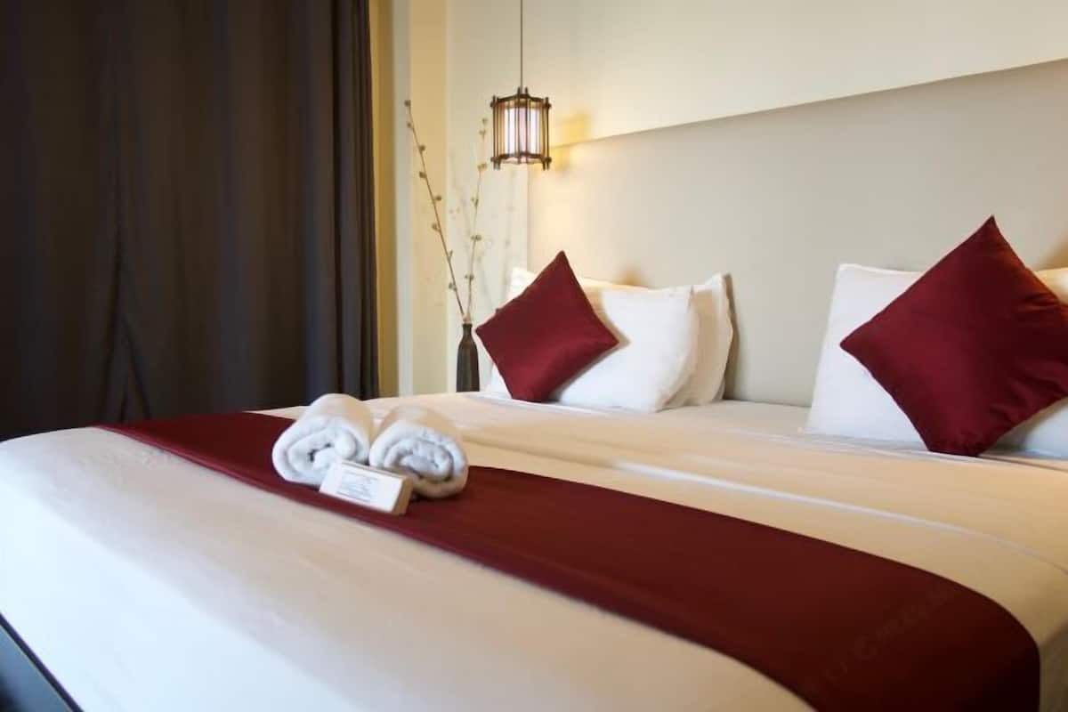A neatly made bed with a red accent pillow, a white pillow, and a decorative hanging light fixture.