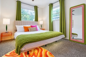 Une chambre d’hôtel avec un lit, des rideaux verts, un miroir et un tapis coloré.